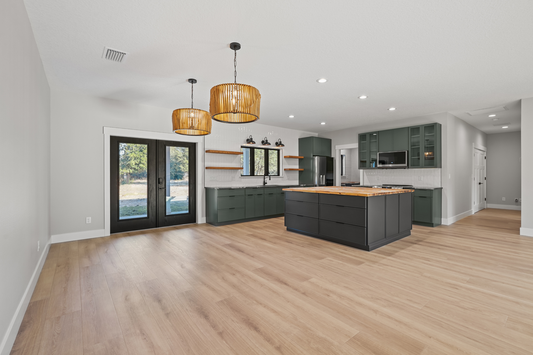 Custom kitchen with sage green cabinets, butcher block island, rattan pendant lights and floating wood shelves