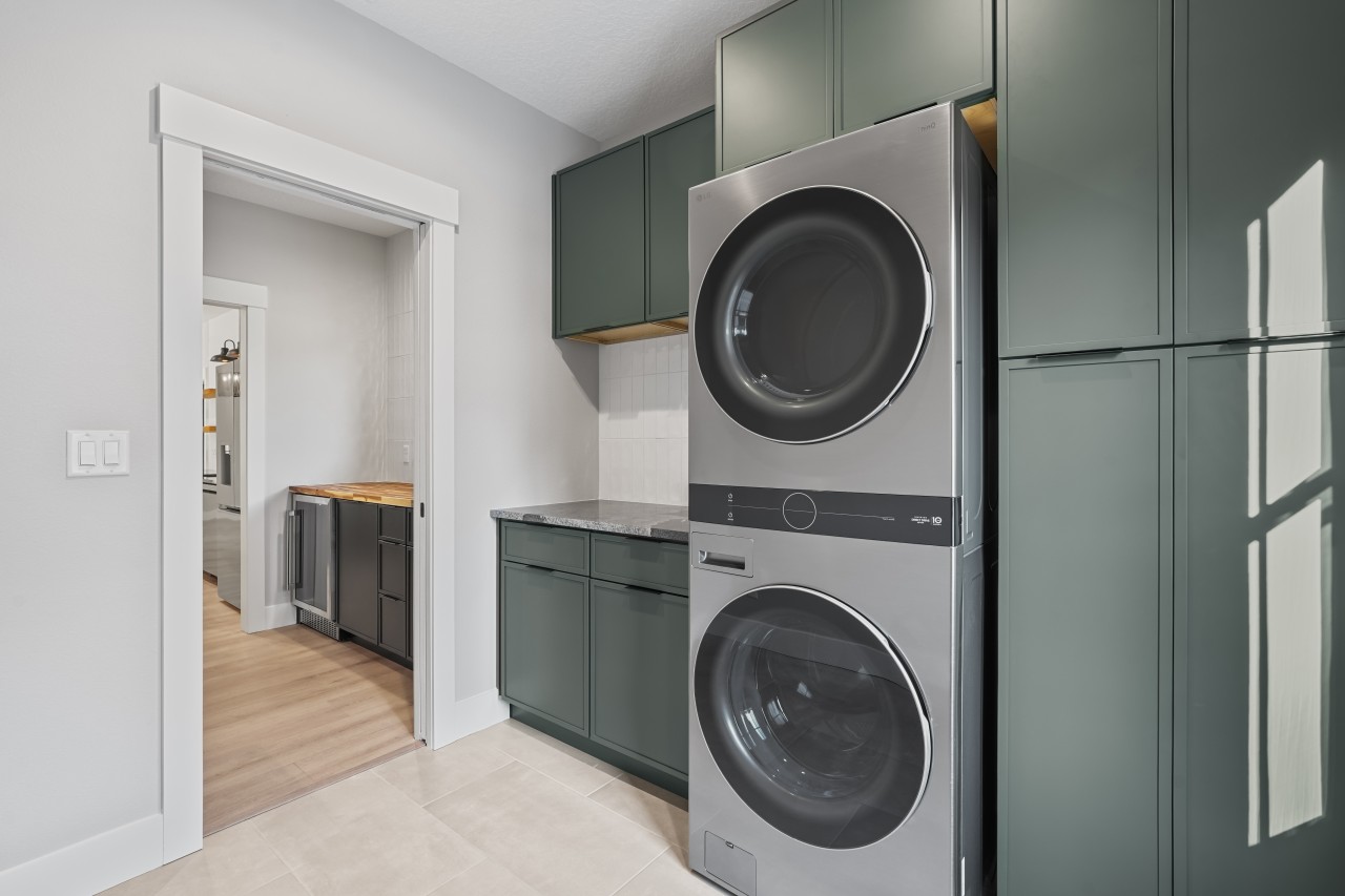 Custom laundry room with stacked front-load washer and dryer, dark green cabinets and open doorway to butler's pantry