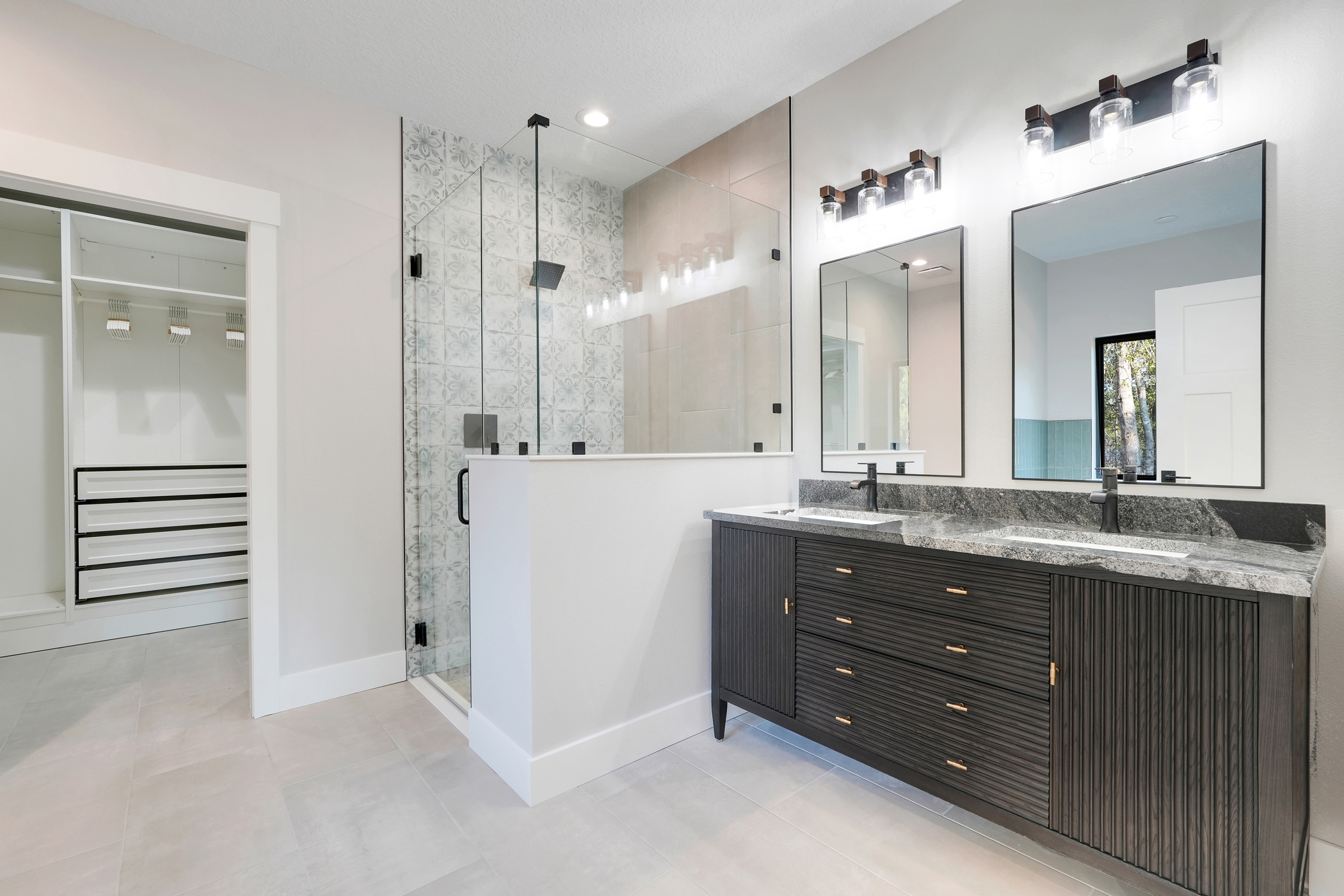 Custom master bathroom with frameless glass walk-in shower, decorative tile, dark wood double vanity and walk-in closet