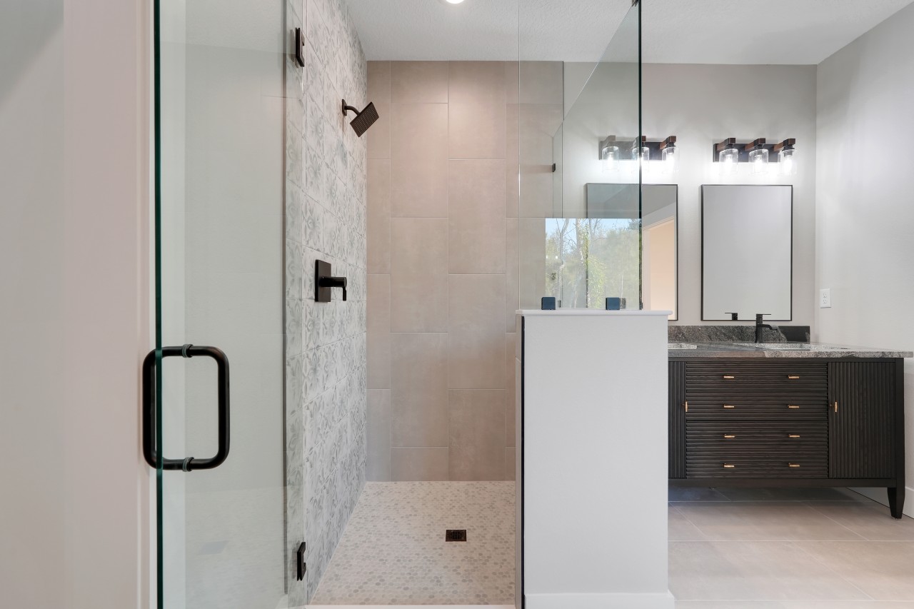 Master bathroom with frameless glass corner shower, decorative tile accent wall, dark fluted wood double vanity and granite countertop