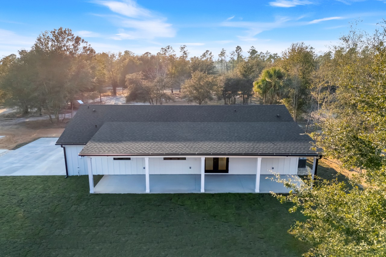 Aerial drone view of newly built white farmhouse home with covered porch and green lawn
