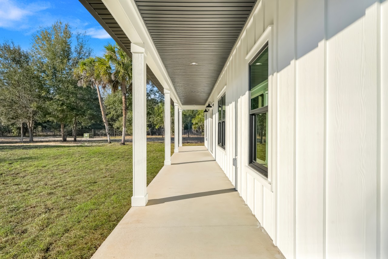 Long covered front porch with white columns along the side of a custom farmhouse home