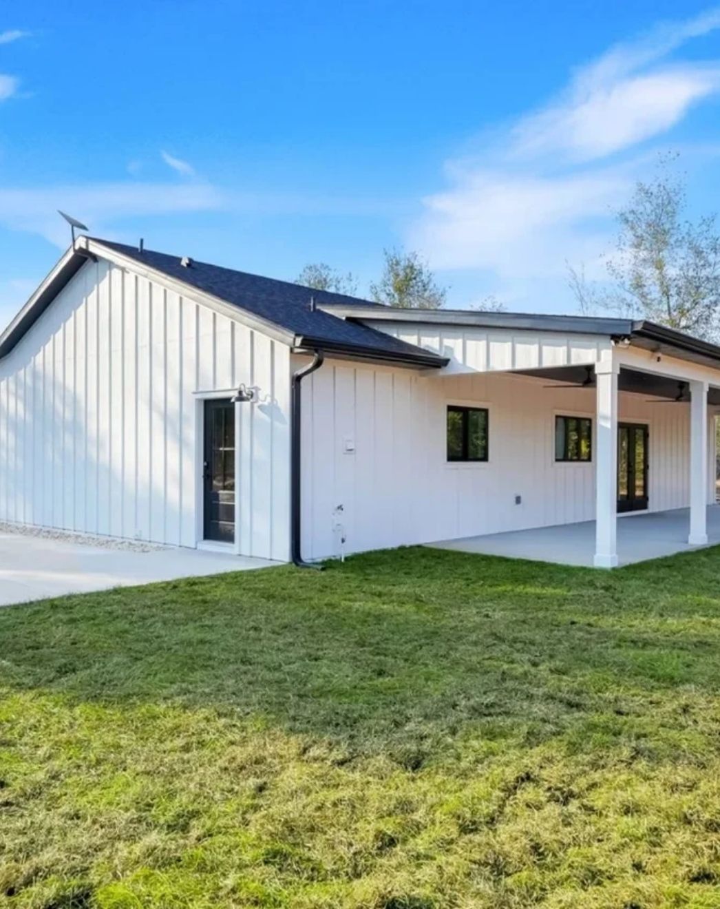 Newly built white farmhouse custom home with covered back porch, black roof and green lawn