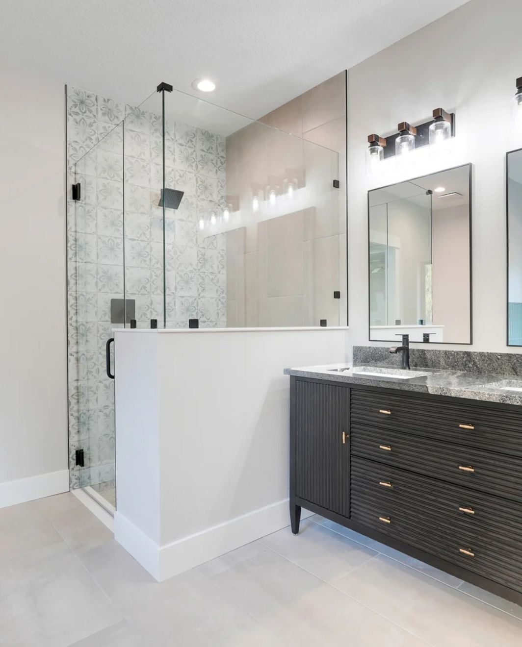 Remodeled master bathroom with frameless glass walk-in shower, decorative tile, dark wood double vanity and granite countertop
