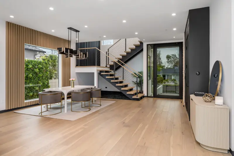 Modern open-concept living and dining area with floating staircase, wood slat accent wall and pendant lighting