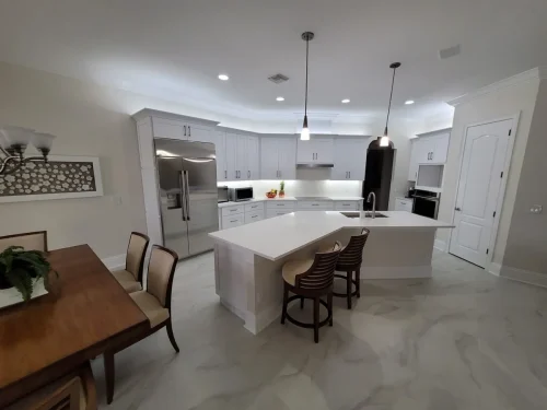Remodeled white kitchen with large center island, pendant lights, bar stools and marble-look tile flooring