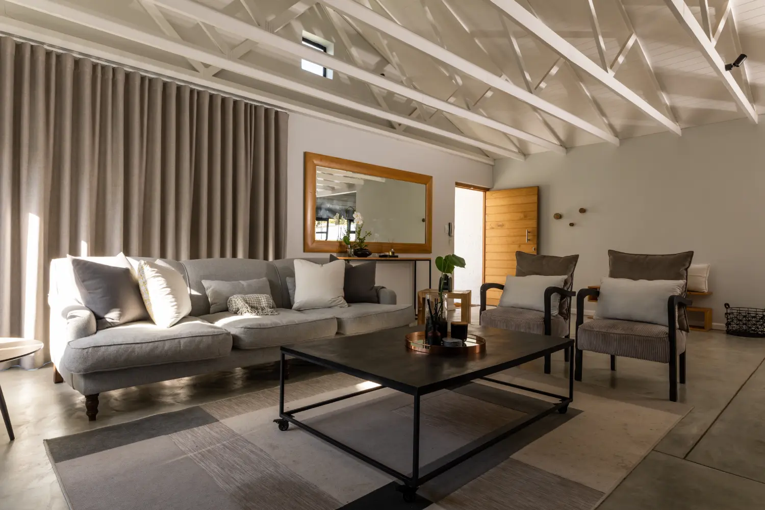 Comfortable living room with gray sectional sofa, armchairs, wooden coffee table and vaulted ceiling with exposed white beams