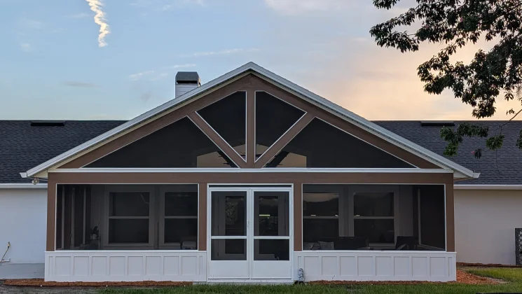 Newly built screened porch addition with gabled roof, large windows and French doors at dusk